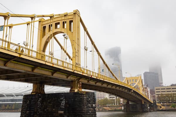 A yellow bridge with a river underneath and tall buildings in the background.