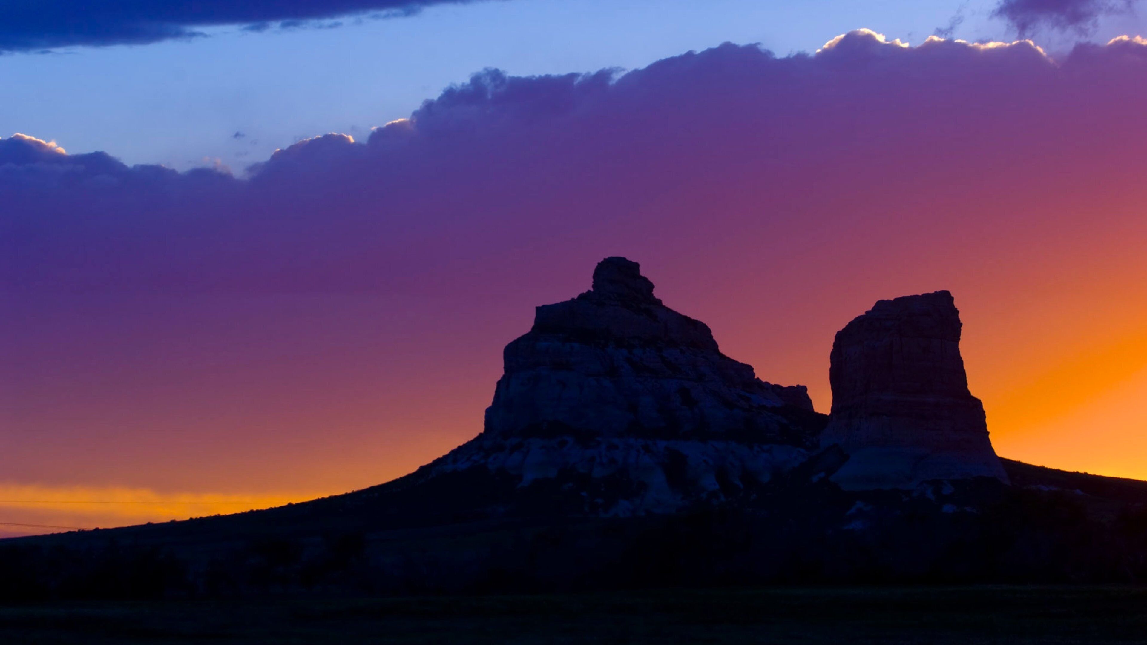 A sunset with two prominent rock formations silhouetted against a colorful sky.