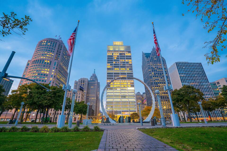A cityscape with modern skyscrapers, a prominent circular sculpture, and American flags.