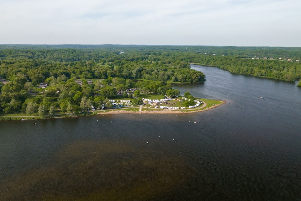 Vista aérea de un camping a orillas de un lago, rodeado de bosque denso.