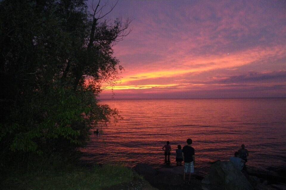 A sunset over a body of water with silhouetted figures on a rocky shore.