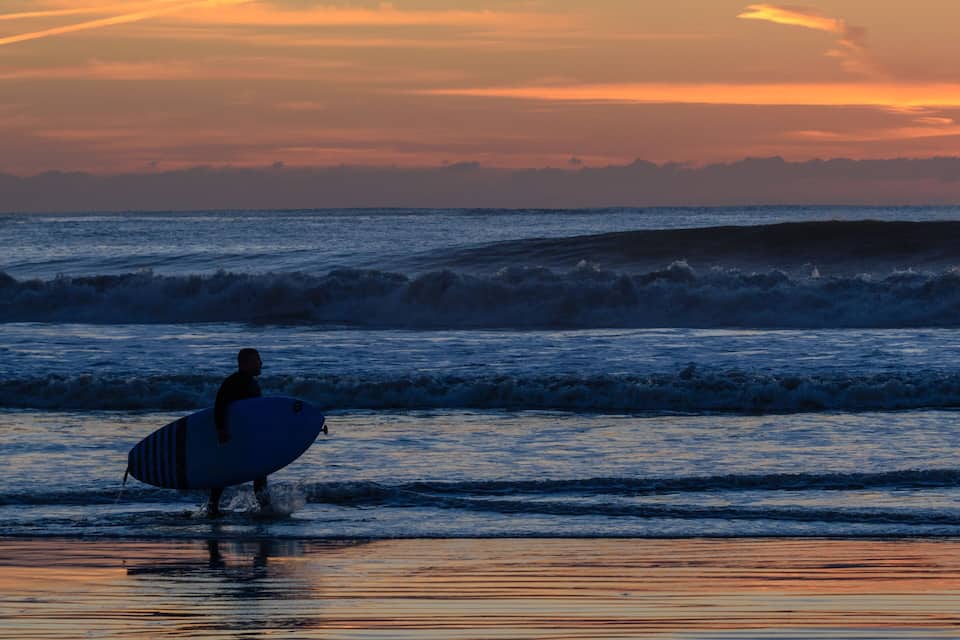 Un surfeur marchant sur la plage au coucher du soleil.