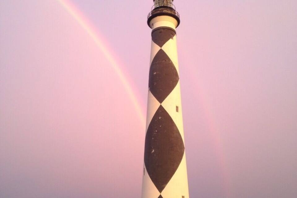 A lighthouse with a diamond pattern, a rainbow, and a forest in the background.