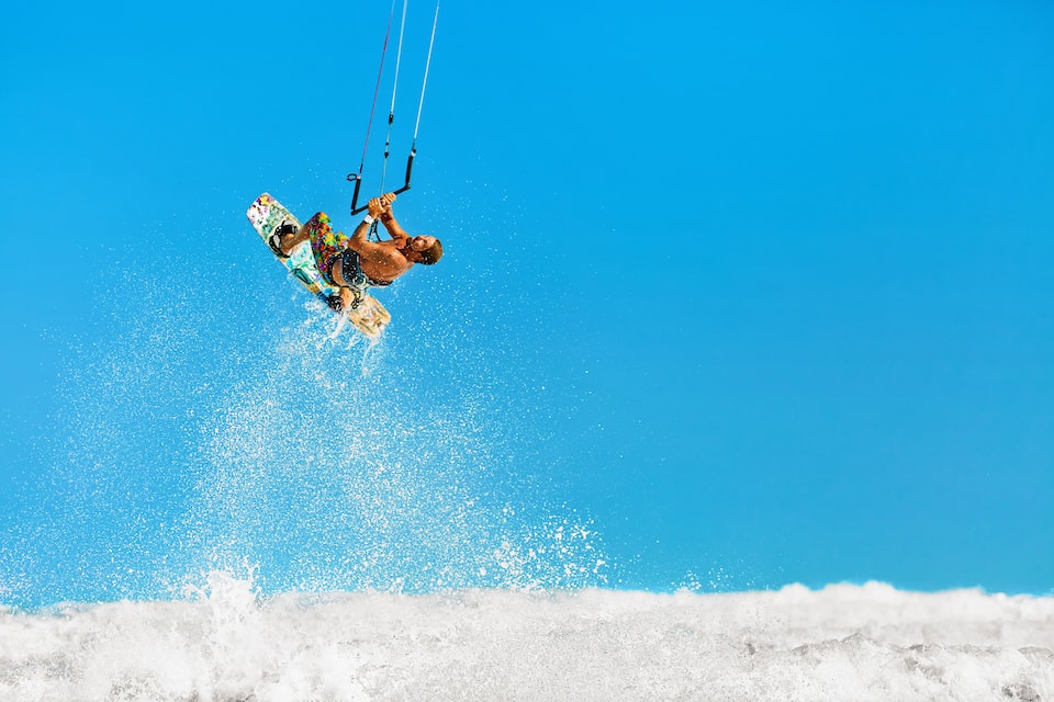 A person kite surfing with a colorful board and ropes against a clear blue sky.