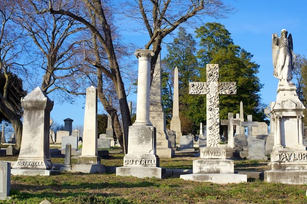 A cemetery with various gravestones, including crosses and statues, surrounded by trees.