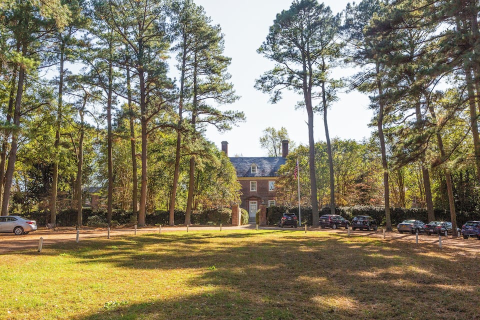 A park with tall trees, a brick building, and parked cars.