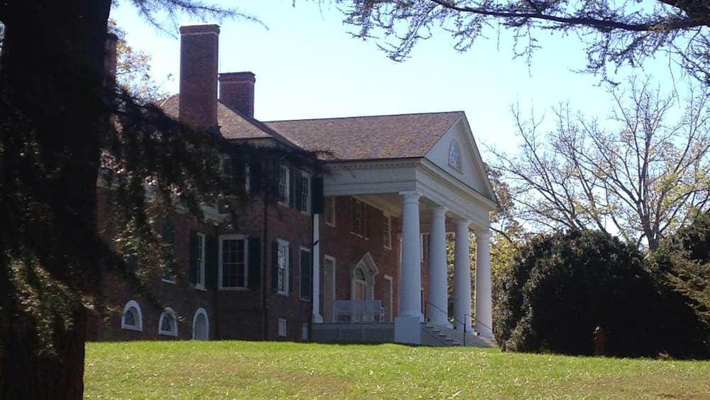 A large brick house with a white porch and columns, surrounded by a grassy lawn and trees.