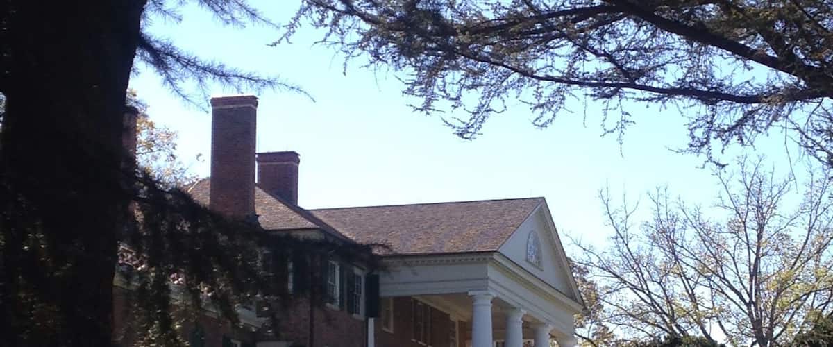 A large brick house with a white porch and columns, surrounded by a grassy lawn and trees.