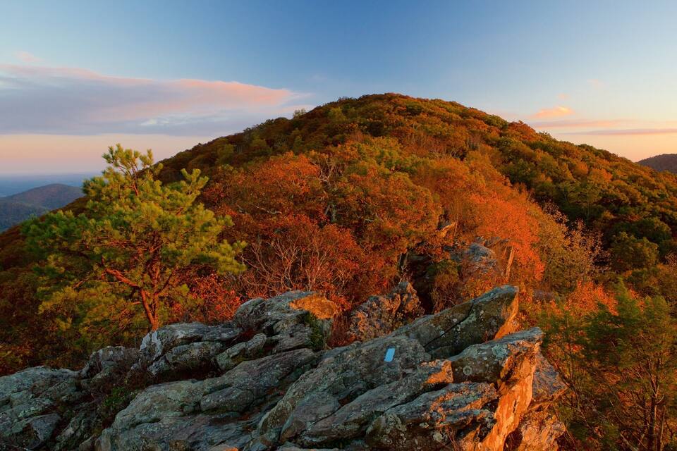 Een bergachtig landschap met herfstkleuren, rotsachtig terrein en een heldere lucht.