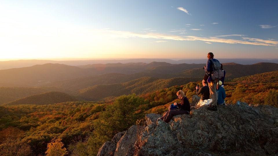 A group of hikers on a mountain ridge with autumn foliage and distant mountain ranges.