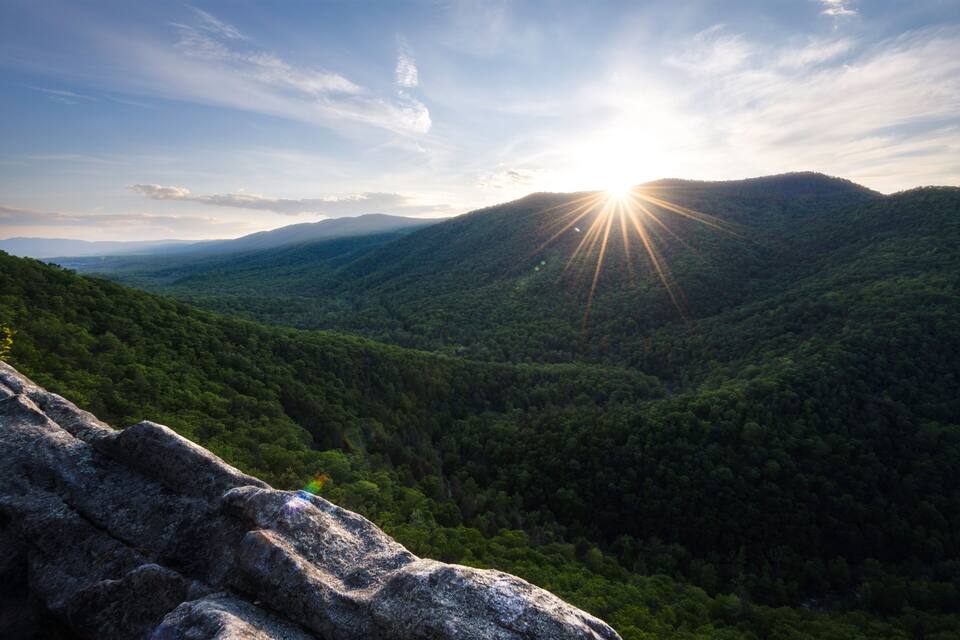 A mountainous landscape with a sun shining over the hills.