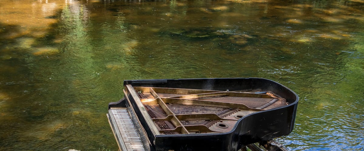 abandoned gran piano, rundown piano by a river bank (Vilnia river) in Uzupis artists quarter in Vilnius, Lithuania, bohemian atmosphere. Republic of Uzupis