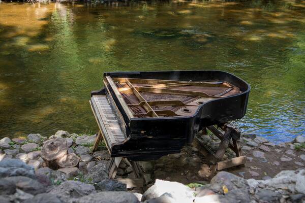 abandoned gran piano, rundown piano by a river bank (Vilnia river) in Uzupis artists quarter in Vilnius, Lithuania, bohemian atmosphere. Republic of Uzupis