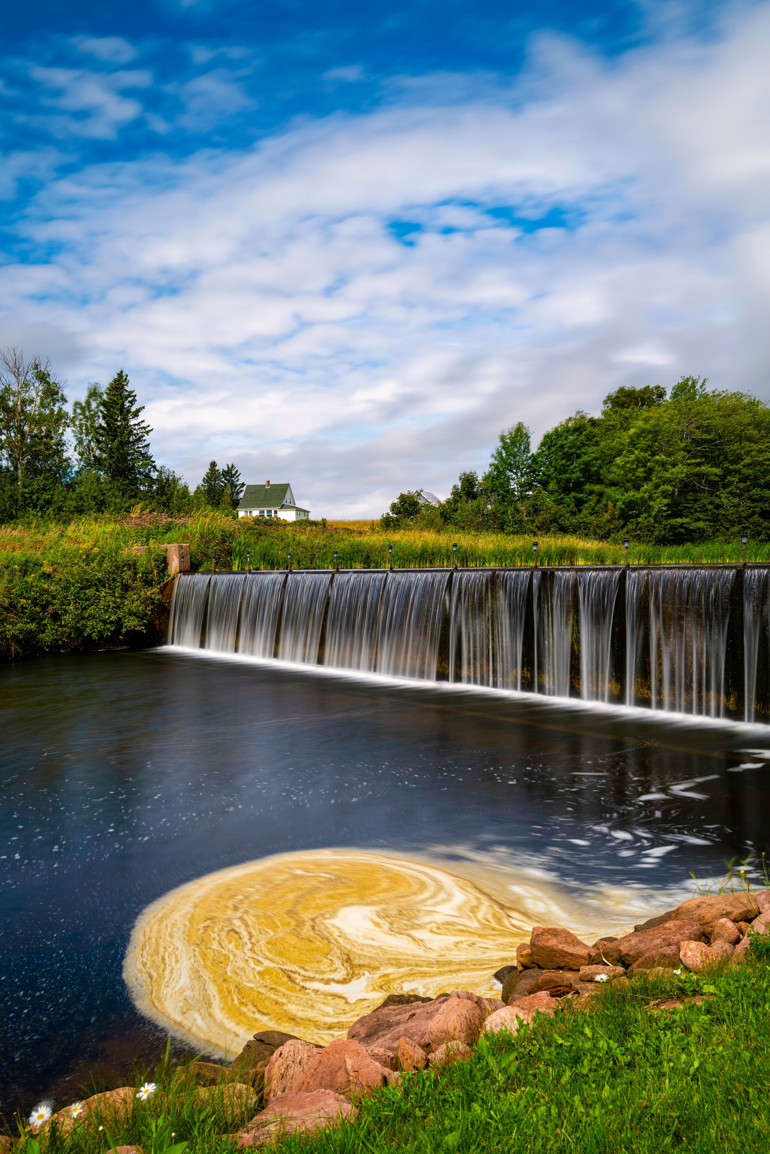 Tranquil Glenwood Pond landscape with water dam, green forest hill, and white summer cloudscape in Prince Edward Island, Canada