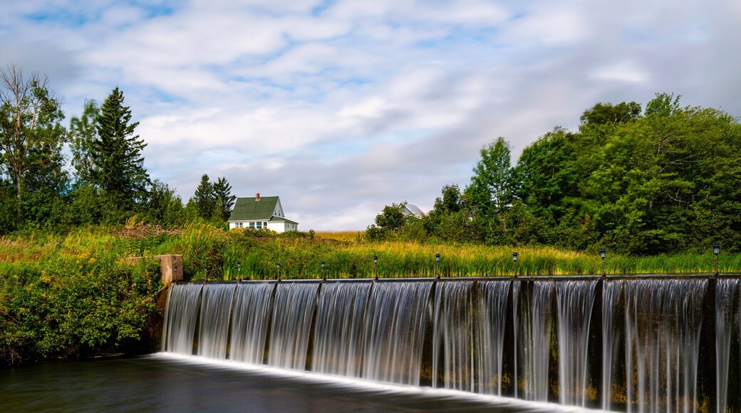 Tranquil Glenwood Pond landscape with water dam, green forest hill, and white summer cloudscape in Prince Edward Island, Canada