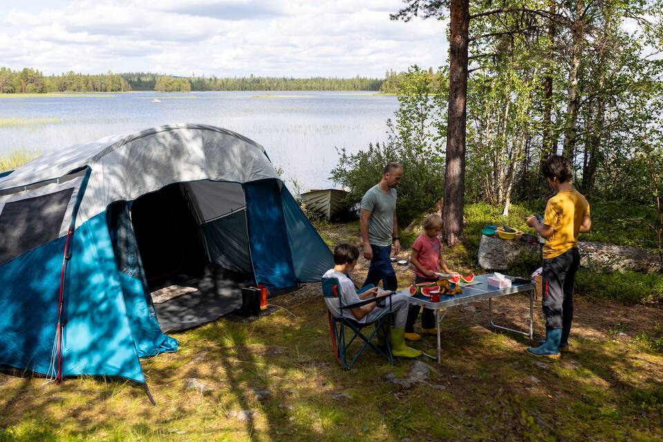 Une scène de camping au bord d’un lac, avec des tentes et une table garnie de nourriture.