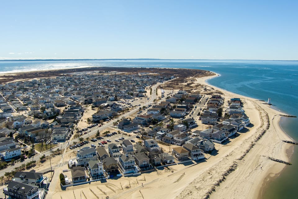 A coastal residential area with houses along the beach and a lighthouse in the distance.