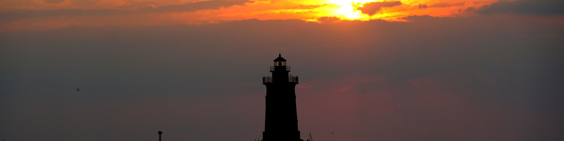 Silhouette of a light house and a man on a paddle board during sunset at Cape Henlopen State Park, Lewes, Delaware, U.S.A