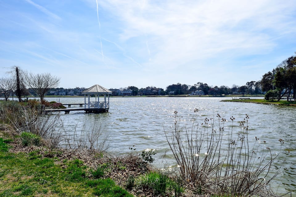 A lake with a gazebo on a dock, surrounded by grass and trees.