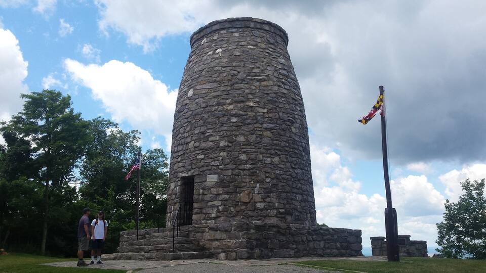 A stone tower with a flagpole, surrounded by trees and a cloudy sky.