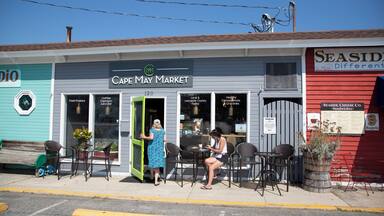 Uma rua com um café chamado Cape May Market, com mesas ao ar livre e uma placa para Seaside Cheese Co.