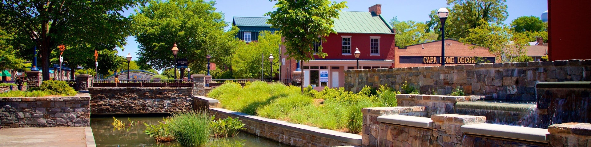 A canal with water lilies, a stone bridge, and a red building with a green roof.