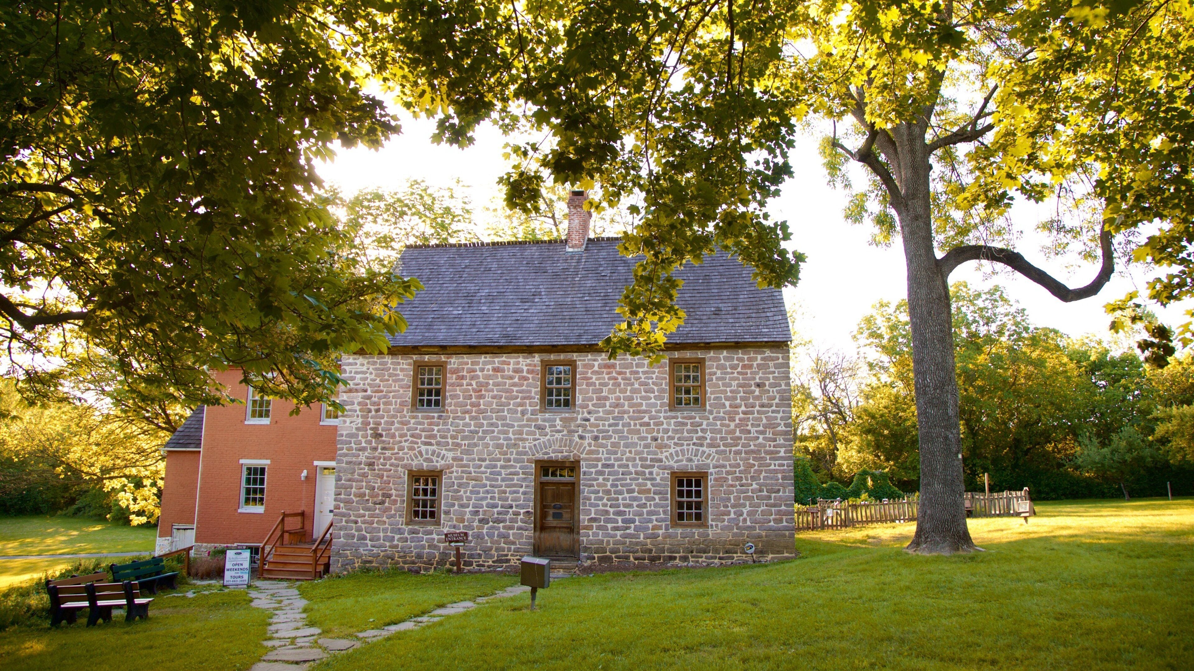A stone building with a red brick section, surrounded by trees and a grassy lawn.