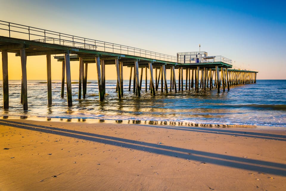 A pier extending into the ocean with a sandy beach in the foreground.