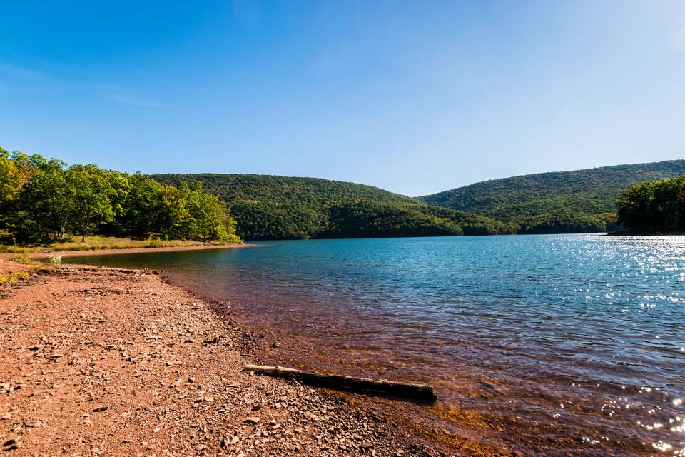 A clear lake with a rocky shoreline and forested hills in the background.