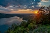 A sunset over a calm lake surrounded by forested hills.