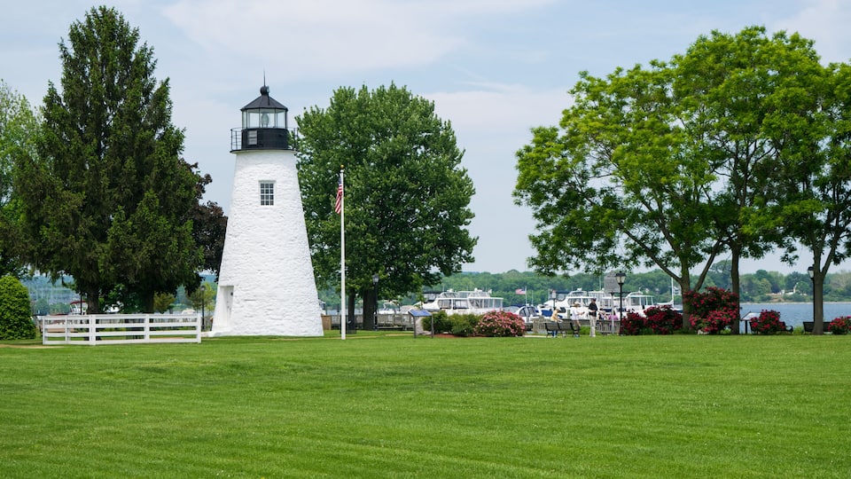 A white lighthouse with a black top, surrounded by lush green grass and trees.