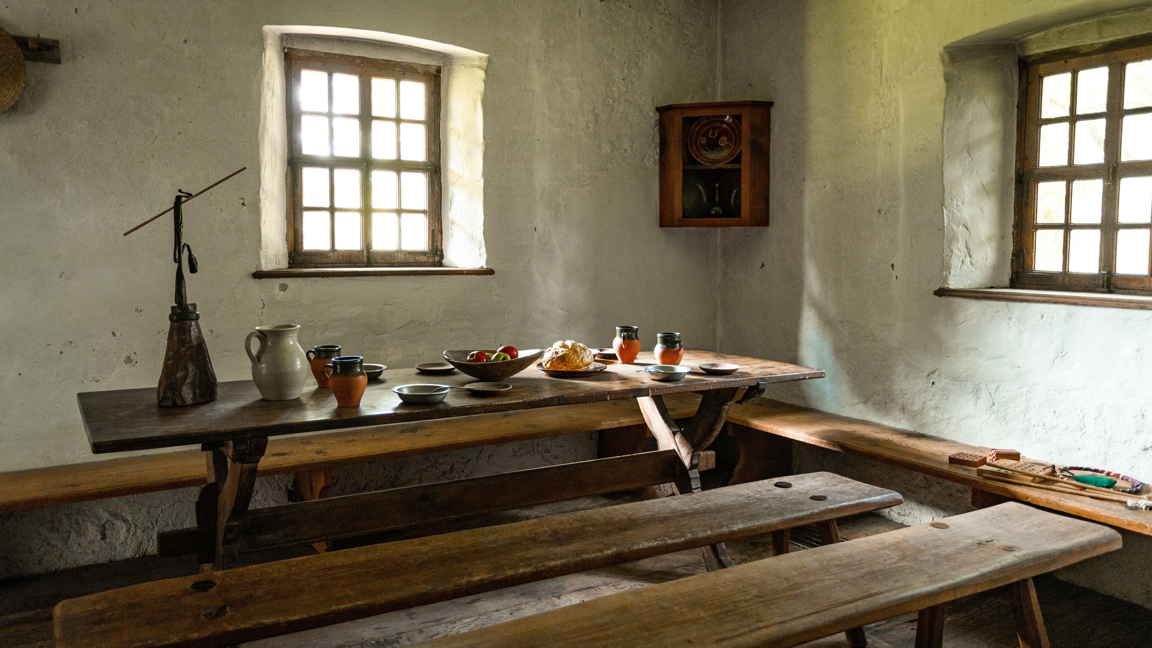 A rustic wooden table with benches, a window, and various kitchen utensils.