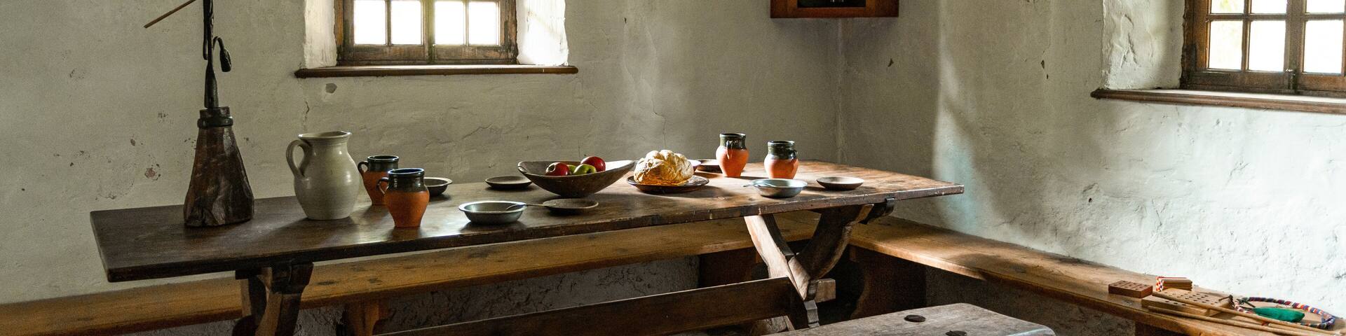 A rustic wooden table with benches, a window, and various kitchen utensils.