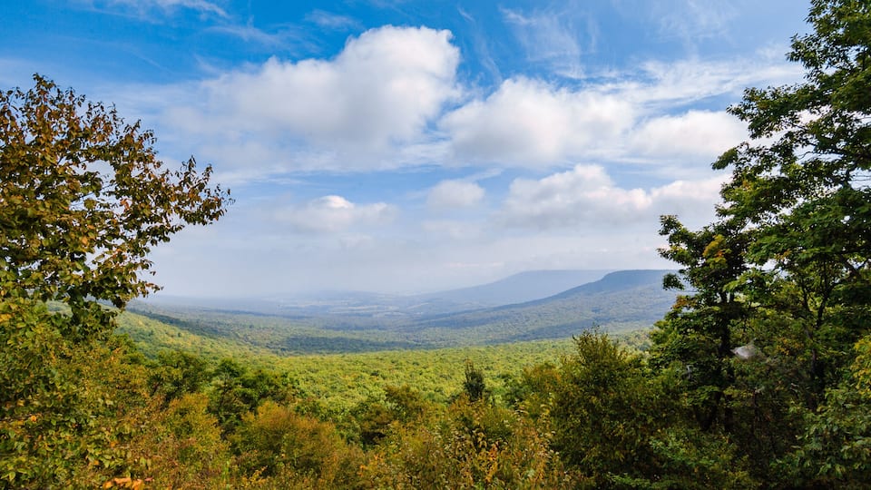 A lush green valley with mountains in the distance and a partly cloudy sky.