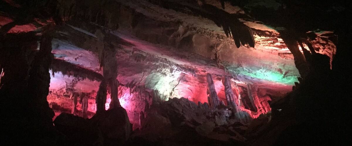 A cave with colorful lighting highlighting stalactites and stalagmites.