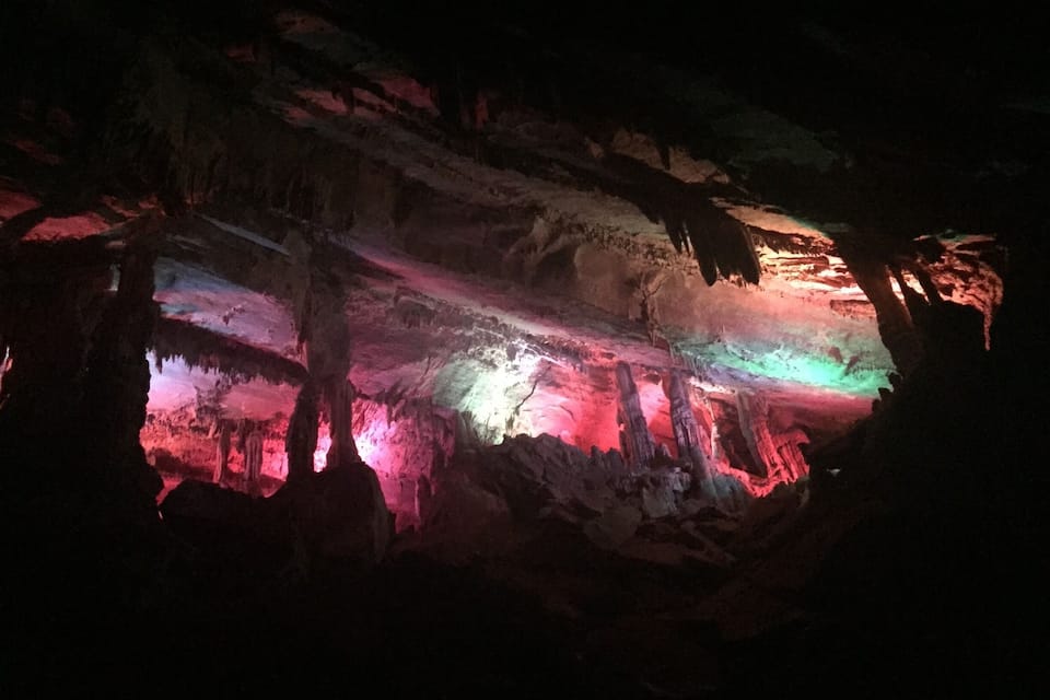Caverna com iluminação colorida realçando estalactites e estalagmites.