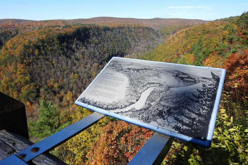 A map of Pine Creek on a metal sign, surrounded by autumn-colored foliage.