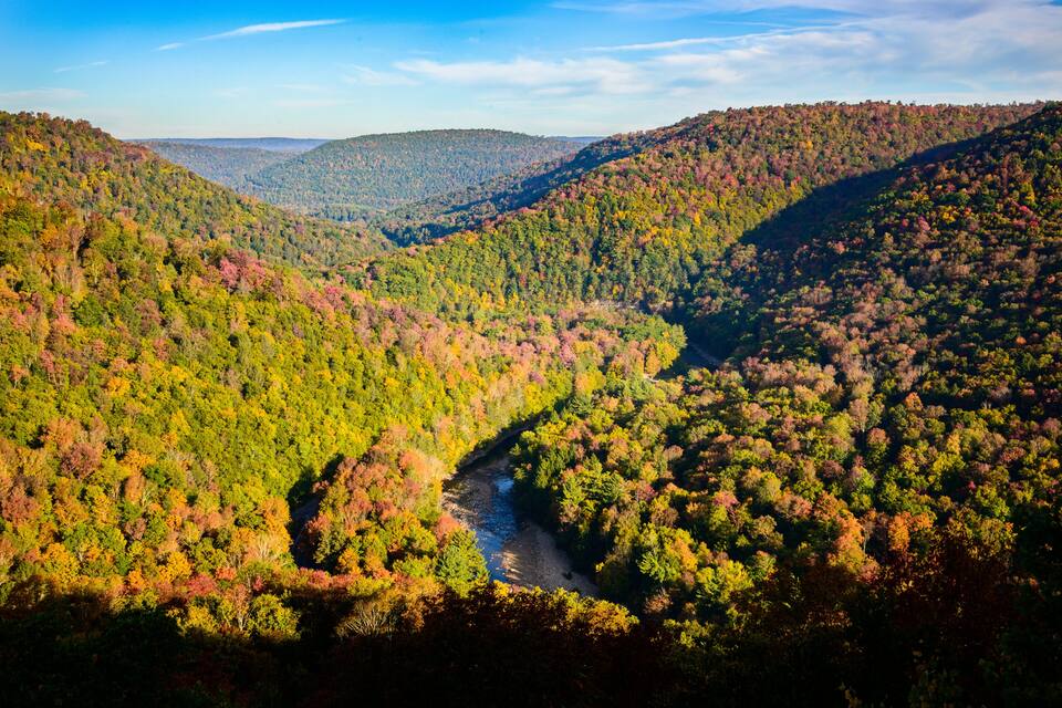 A valley with a river, surrounded by hills covered in autumn foliage.