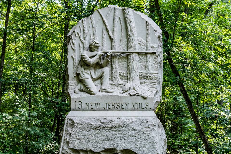 A stone monument with a soldier holding a rifle, surrounded by trees.