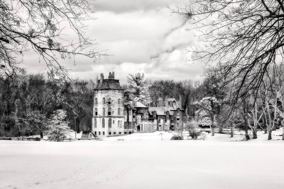 A snow-covered landscape with a historic castle surrounded by trees.