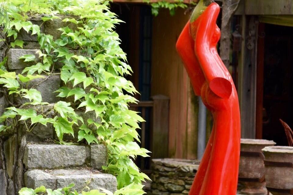 A statue of a woman in a red dress standing by a stone wall with green ivy.