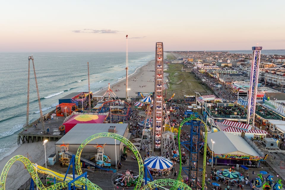 A coastal amusement park with roller coasters, a Ferris wheel, and a beach.