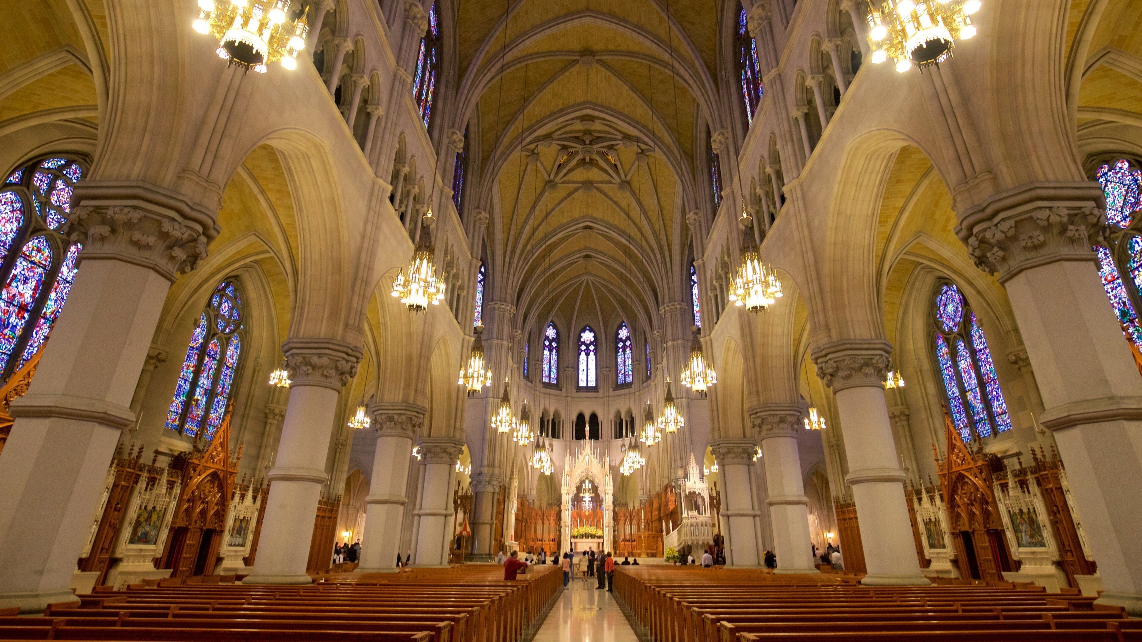A cathedral interior with high vaulted ceilings, stained glass windows, and ornate chandeliers.