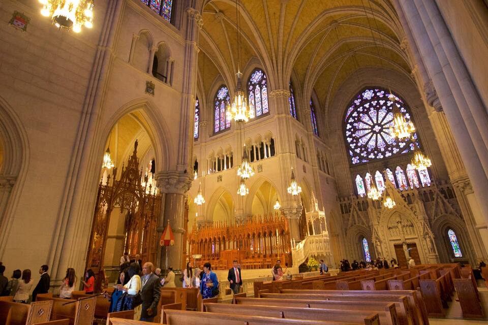 A cathedral interior with high vaulted ceilings, stained glass windows, and rows of pews.