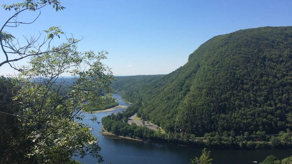 A river winding through a densely forested valley with a steep hillside on one side and a clear blue sky above.