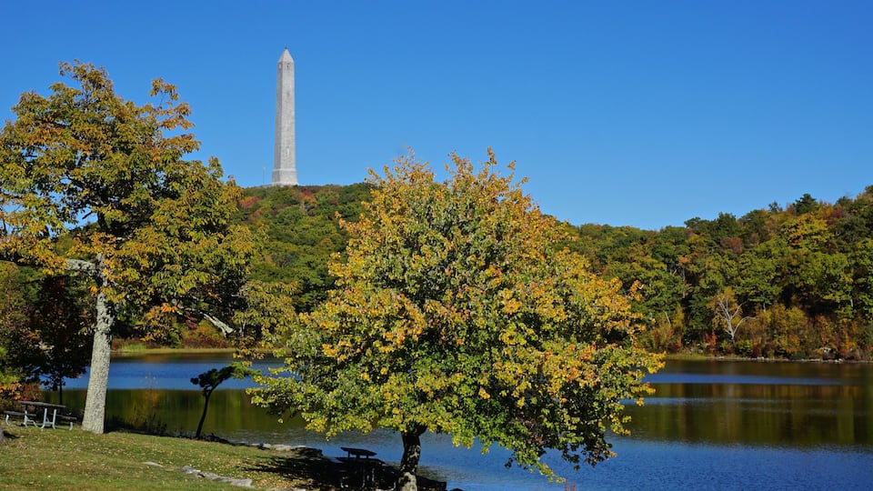 A lake with a monument in the background and autumn foliage in the foreground.