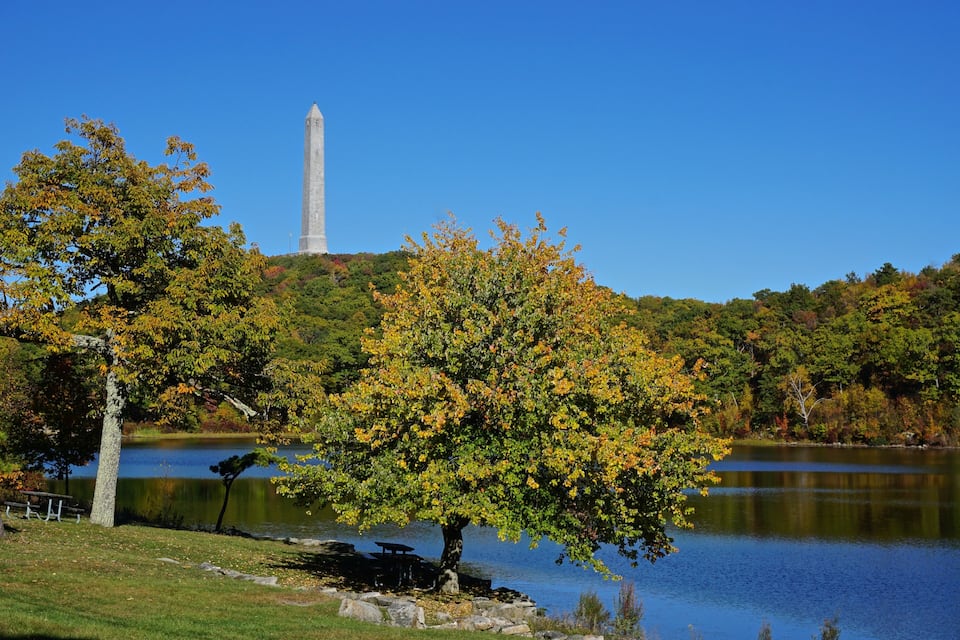 A lake with a monument in the background and autumn foliage in the foreground.