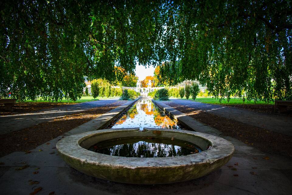 Un jardin symétrique avec une fontaine centrale, entouré d’arbres et bordé d’un sentier.