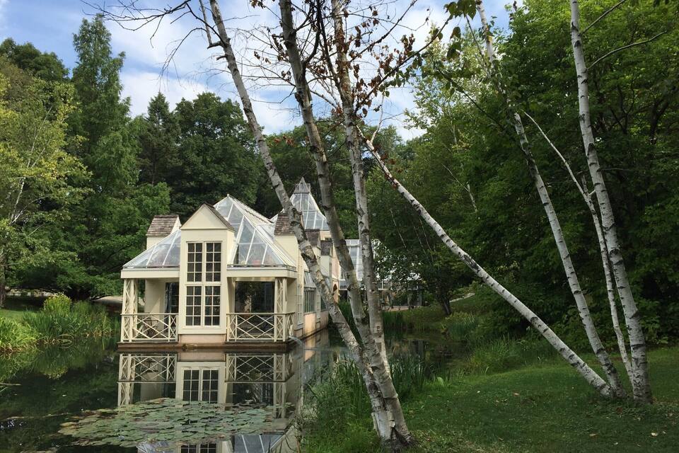 A house with a glass conservatory by a pond surrounded by trees.