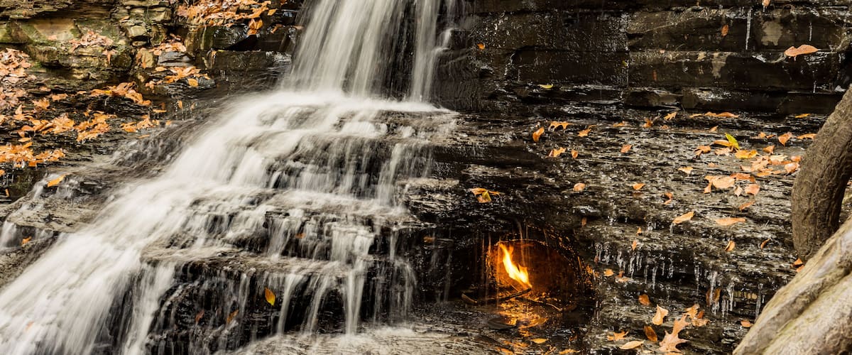 A waterfall cascading over rocky terrain with autumn leaves scattered around.